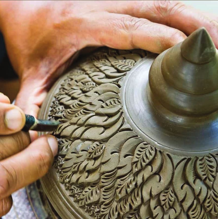 A potter carving a leaf pattern into a clay lid with a fine tool